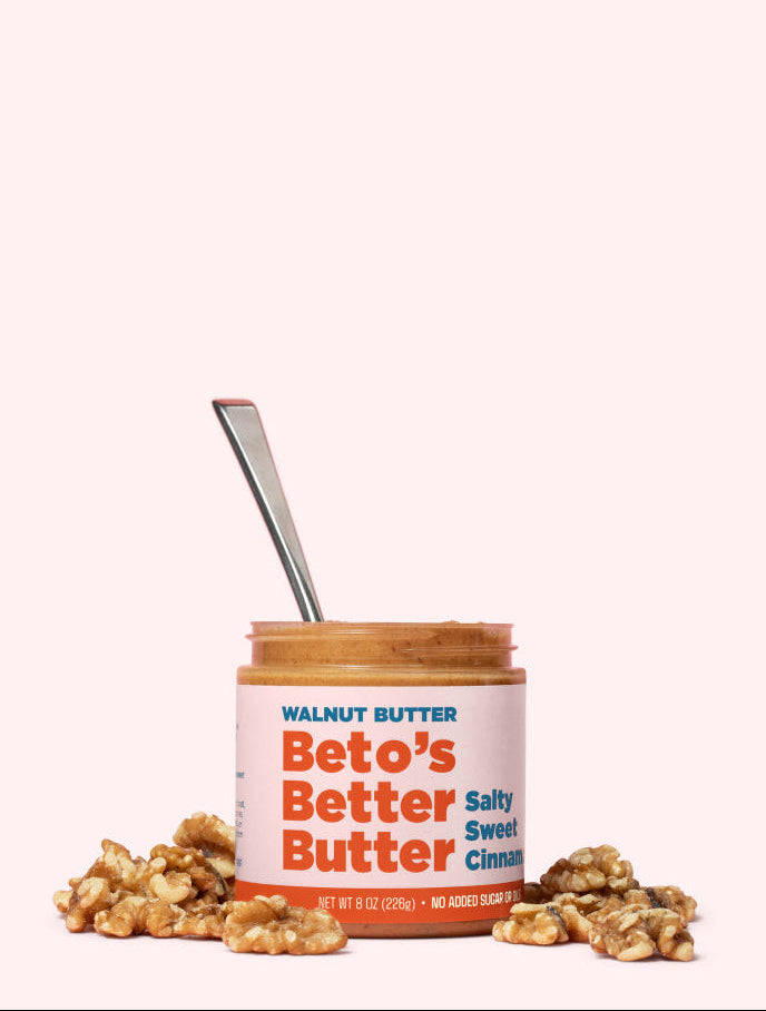 Jar of Beto's Better Butter with a spoon and walnuts on a white background