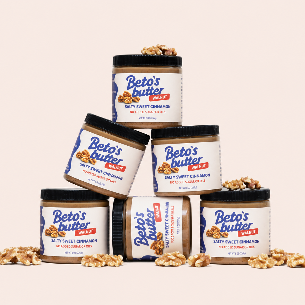 Stack of 6 jars of Beto's Butter with walnuts scattered on a light pink background